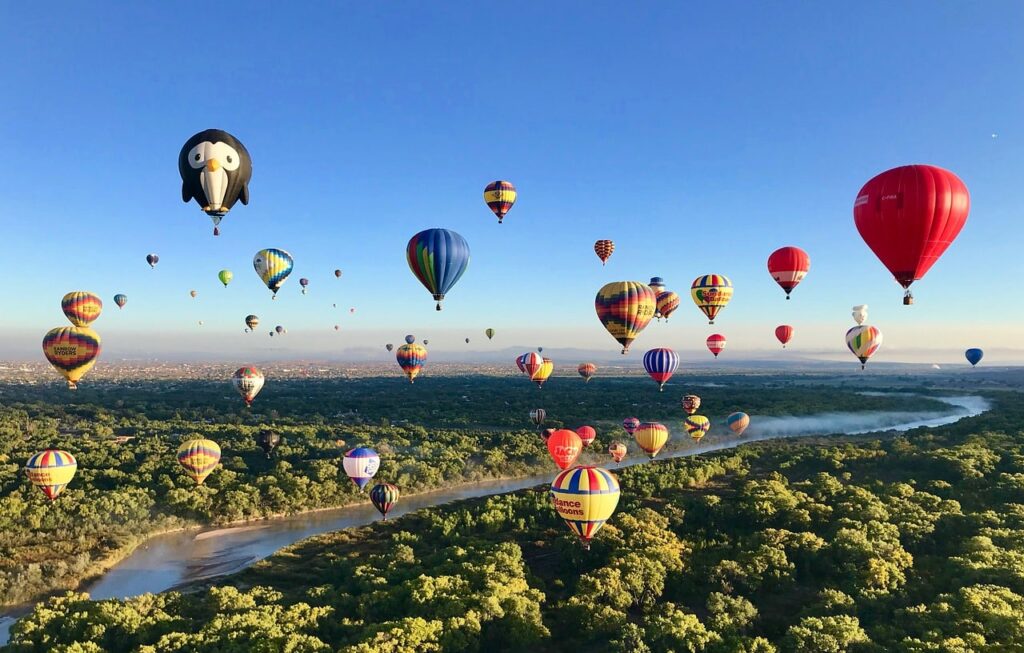 A bunch of hot air balloons flying over the trees